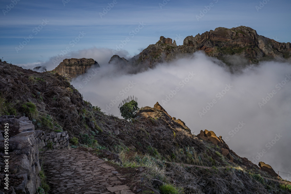 Trail leading towards Pico do Areeiro, Madeira island's third highest peak, with the mountain range peaks in the clouds, Portugal; Sao Roque do Faial, Madeira, Portugal