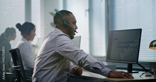 Картината върху платно Modern call center office: African American consultant sits down at computer, puts on headset, uses computer