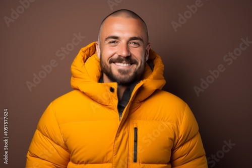 Portrait of a smiling man in his 30s donning a durable down jacket in front of plain cyclorama studio wall