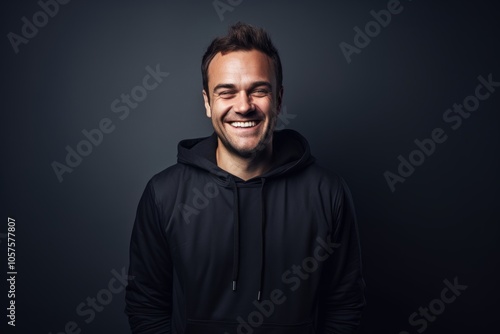 Portrait of a grinning man in his 30s wearing a zip-up fleece hoodie over plain cyclorama studio wall