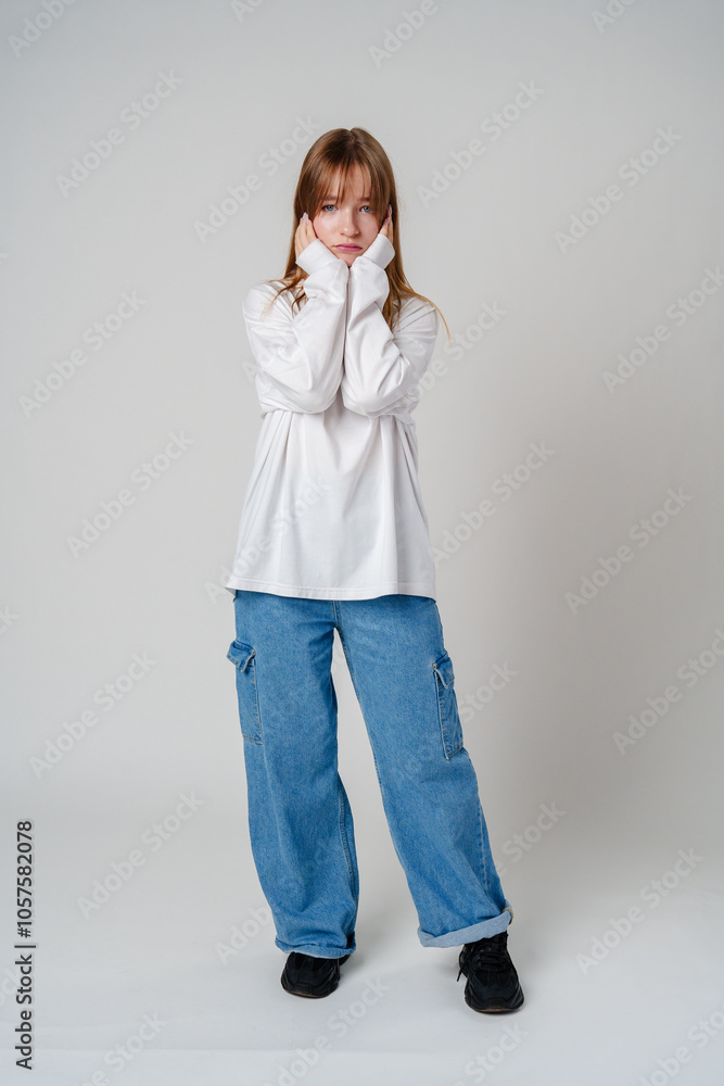 A young girl in a white sweatshirt shows a thoughtful expression against a plain background A young girl in a white sweatshirt shows a thoughtful expression against a plain background