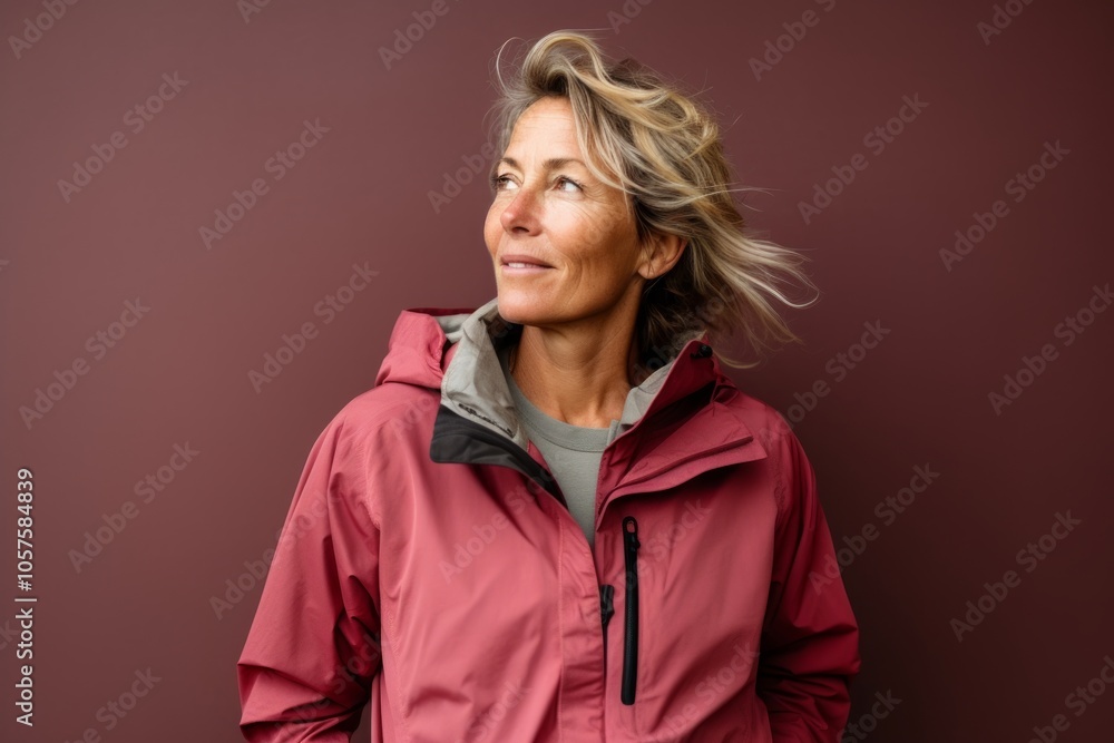 Portrait of a blissful woman in her 50s wearing a functional windbreaker in plain cyclorama studio wall