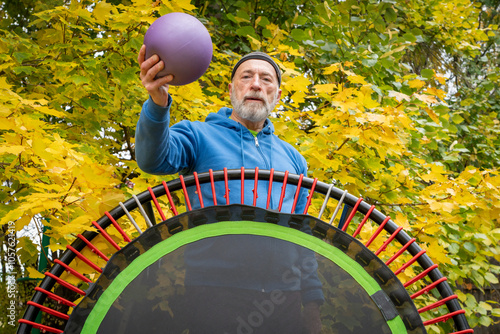 senior man with a medicine ball and a mini trampoline for fitness exercising and rebounding, fall backyard  scenery photo