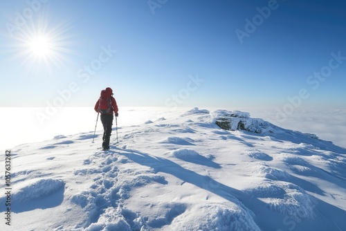 A lone hiker ascends a snow-covered mountain peak, with a bright sun shining above and a sea of clouds below.