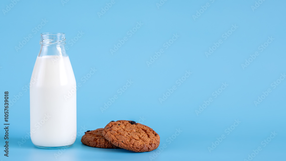 A bottle of milk next to chocolate oatmeal cookies on blue background. Place for text. A bottle of milk next to chocolate oatmeal cookies on blue background. Place for text.