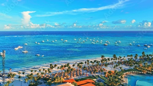 Luxury beach resort hotel, drone shot. Swimming pool and sun loungers, umbrellas under palm trees. Summer evening on the coast, tourist vacation background. Blue sea with white yachts.