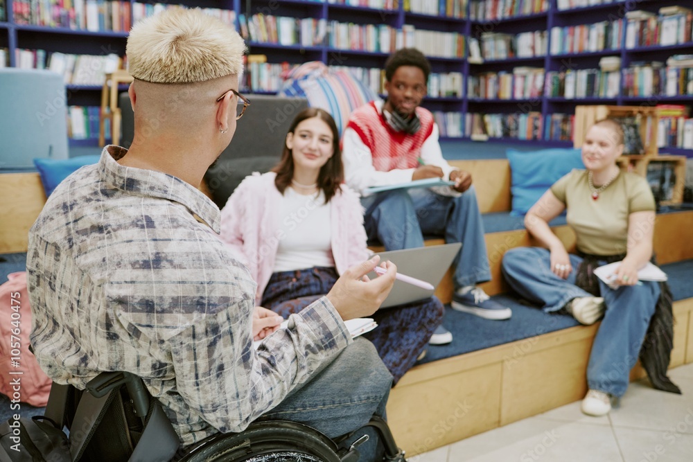 Fototapeta premium Group of diverse students sitting in modern library engaged in study session on tiered seating. One student in wheelchair, all focused and interacting, surrounded by shelves of books