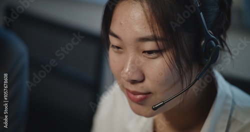 Call center office: Close up portrait of Asian female technical customer support specialist talking on headset, working on computer, providing online assistance for client. Hotline operator working. photo