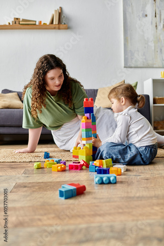 A delighted plus size woman and her daughter create a colorful block tower on the floor. photo