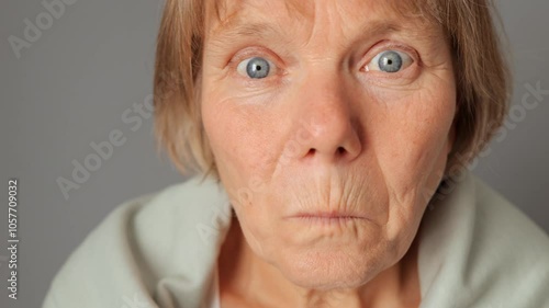 Surprised mature woman gazing steadily taking off her glasses displaying curious shocked reaction evaluates strange situation with scrupulous attention isolated over gray background
