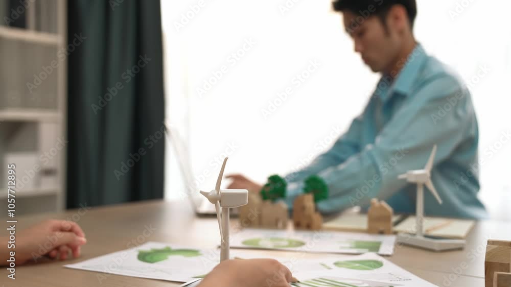 Businesswoman hold windmill model represented using clean energy. Wooden block symbolized ecology house and green power graph scatter around on the table, businessman working on laptop. Delineation. Businesswoman hold windmill model represented using clean energy. Wooden block symbolized ecology house and green power graph scatter around on the table, businessman working on laptop. Delineation.