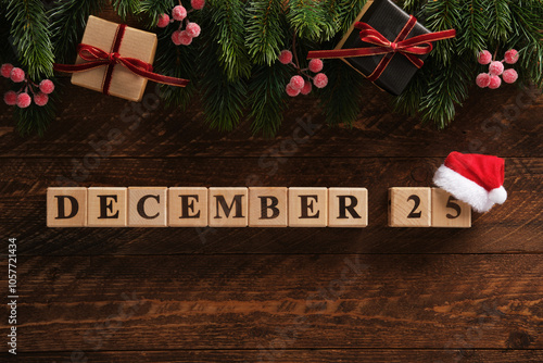 Date December 25 on dark wooden background with spruce sprigs, gift boxes with red ribbons, red berries. Festive background.