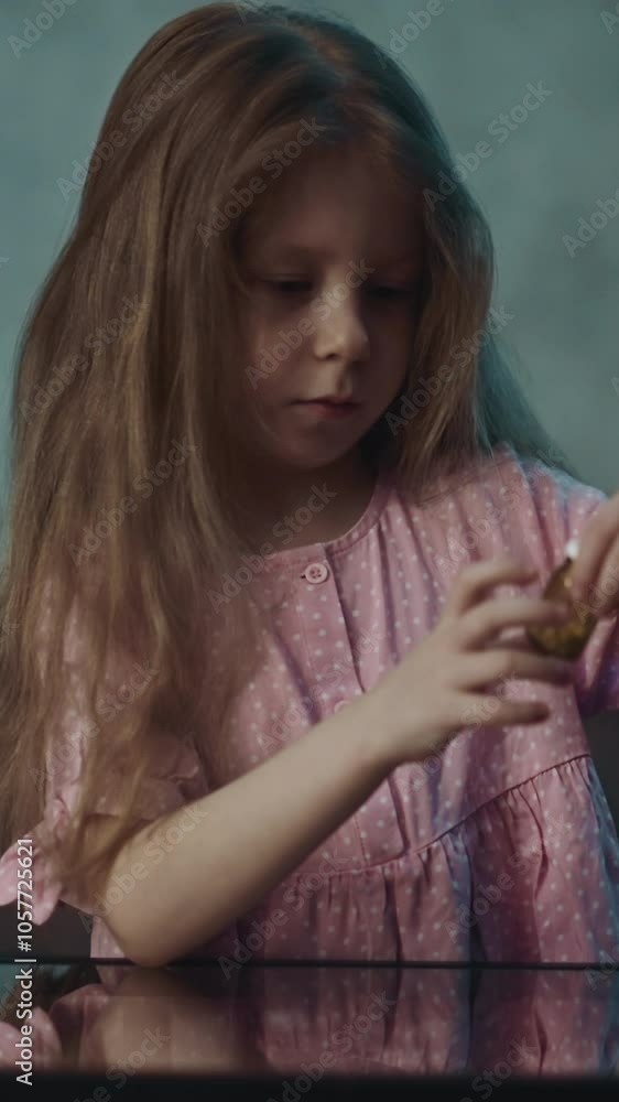 Cute curious naughty little girl takes drug bottle full of white vitamin pills sitting at small glass table in semi-dark room at home close view slow motion Cute curious naughty little girl takes drug bottle full of white vitamin pills sitting at small glass table in semi-dark room at home close view slow motion