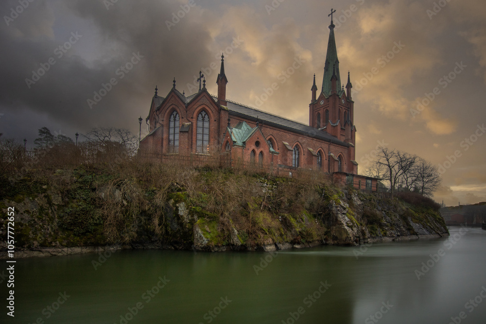 Historical landmark, the church made of red brick. Located on a river on an island. Photographed in bad weather at sunset by the river in Trollhättan, Sweden, Scandinavia Historical landmark, the church made of red brick. Located on a river on an island. Photographed in bad weather at sunset by the river in Trollhättan, Sweden, Scandinavia