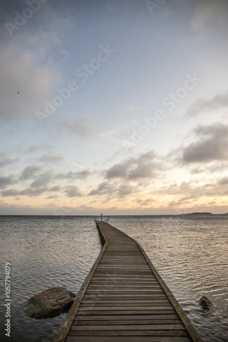 Sunrise over a lake in autumn. A wooden jetty protrudes into the water while grass has established itself on the sandy beach. The lake and beach, located on Lake Vänern in Näs Sannar, Sweden, Scandina