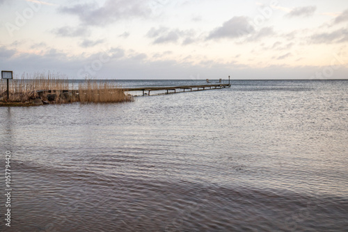 Sunrise over a lake in autumn. A wooden jetty protrudes into the water while grass has established itself on the sandy beach. The lake and beach, located on Lake Vänern in Näs Sannar, Sweden, Scandina photo