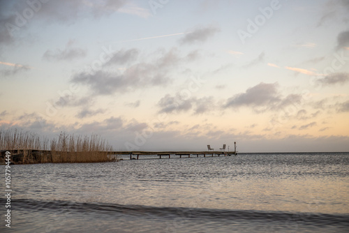 Sunrise over a lake in autumn. A wooden jetty protrudes into the water while grass has established itself on the sandy beach. The lake and beach, located on Lake Vänern in Näs Sannar, Sweden, Scandina