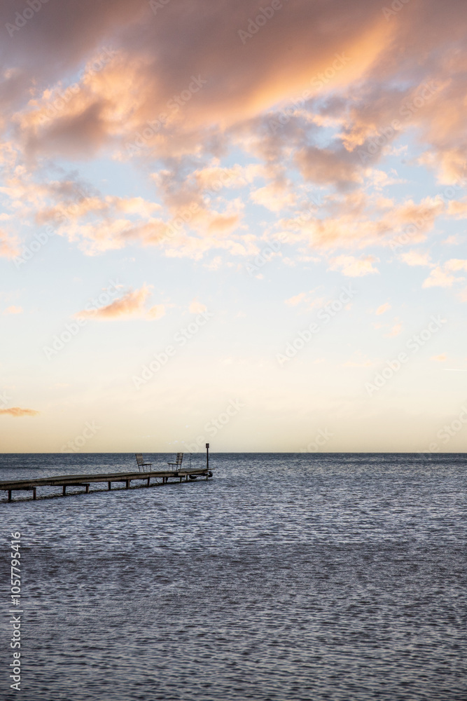 Sunrise over a lake in autumn. A wooden jetty protrudes into the water while grass has established itself on the sandy beach. The lake and beach, located on Lake Vänern in Näs Sannar, Sweden, Scandina Sunrise over a lake in autumn. A wooden jetty protrudes into the water while grass has established itself on the sandy beach. The lake and beach, located on Lake Vänern in Näs Sannar, Sweden, Scandina