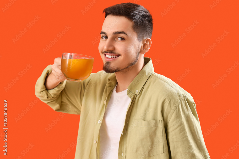 Fototapeta premium Young man with cup of lemon tea on orange background