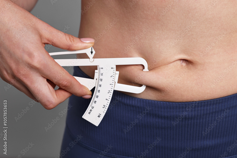 Fototapeta premium Woman measuring body fat with caliper on gray background, closeup