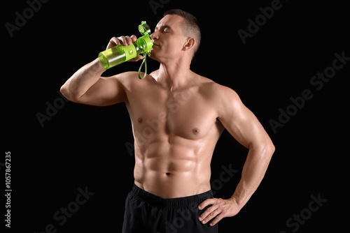 Male bodybuilder drinking water on dark background