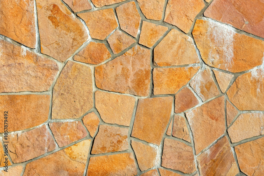 Natural stone wall with textured surface displaying rustic patterns, interlocking shapes, and warm earthy tones, architectural design concept