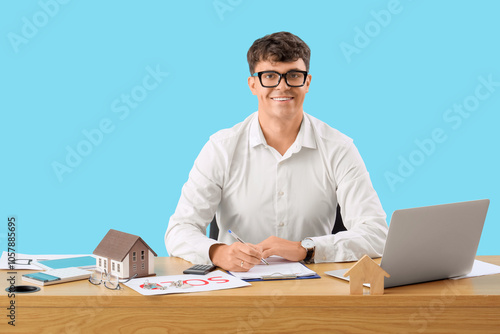 Male real estate agent working at table on blue background