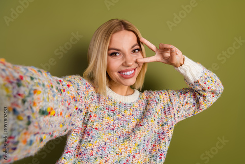 Cheerful young woman in colorful knitwear making playful gesture against khaki background, embodying vibrant fashion and joyful expression. photo