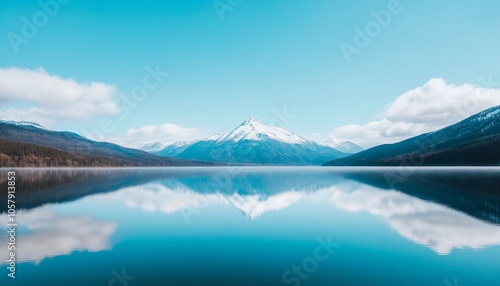 A serene mountain lake scene with a perfect reflection of the snow-capped peak and clouds in the calm, blue water.