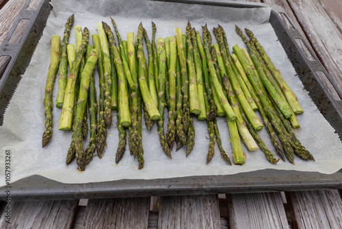 Ein Ofenblech mit gebratenem grünen Spargel auf dem Holztisch. Aufnahme seitlich.