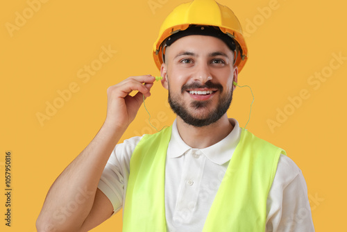 Male builder with earplugs on yellow background, closeup photo