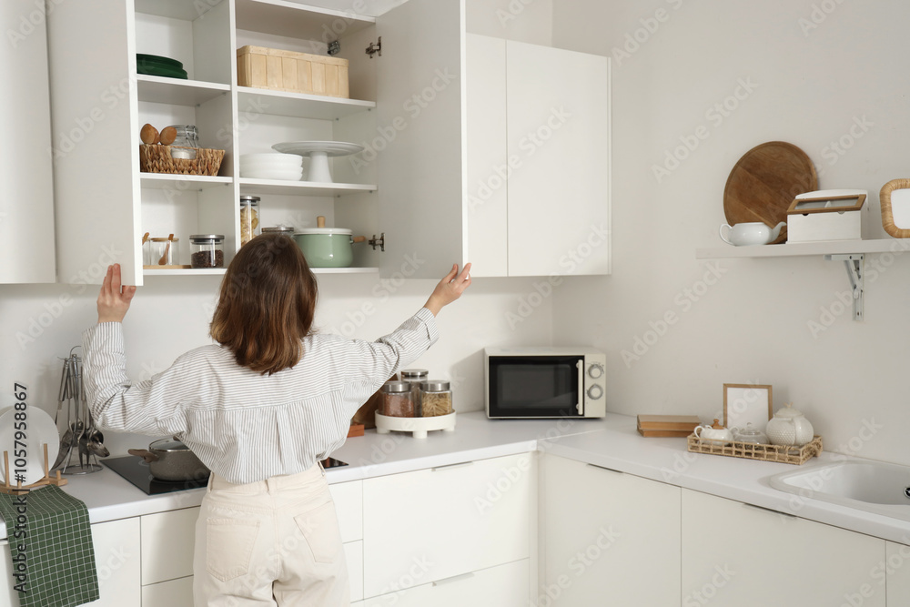 Obraz premium Young woman opening cupboard in kitchen, back view