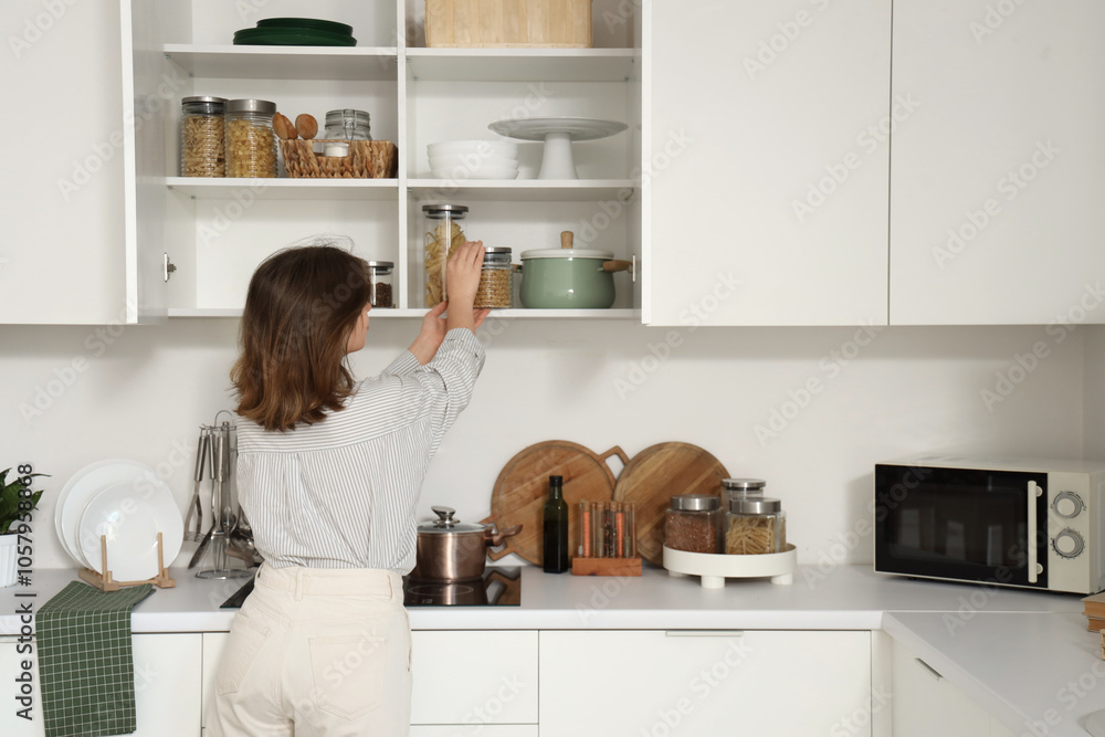 Young woman taking jar from shelf in kitchen, back view Young woman taking jar from shelf in kitchen, back view