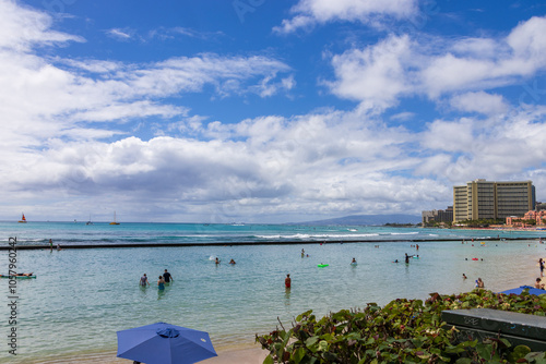 people playing in the ocean water and relaxing in the sand at Waikiki Beach with lush green palm trees and clouds in Honolulu Hawaii USA photo