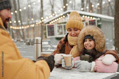 Portrait of happy young family enjoying hot drinks at outdoor cafe table focus on mother and daughter smiling photo