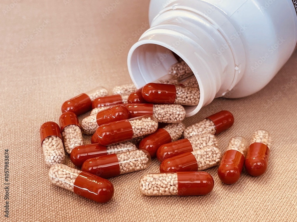 Red and transparent medication capsules pouring from bottle containing pancreatic enzyme