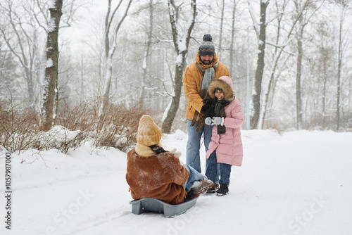 Full length authentic scene of happy family enjoying sledding in winter forest with woman sitting in sled photo