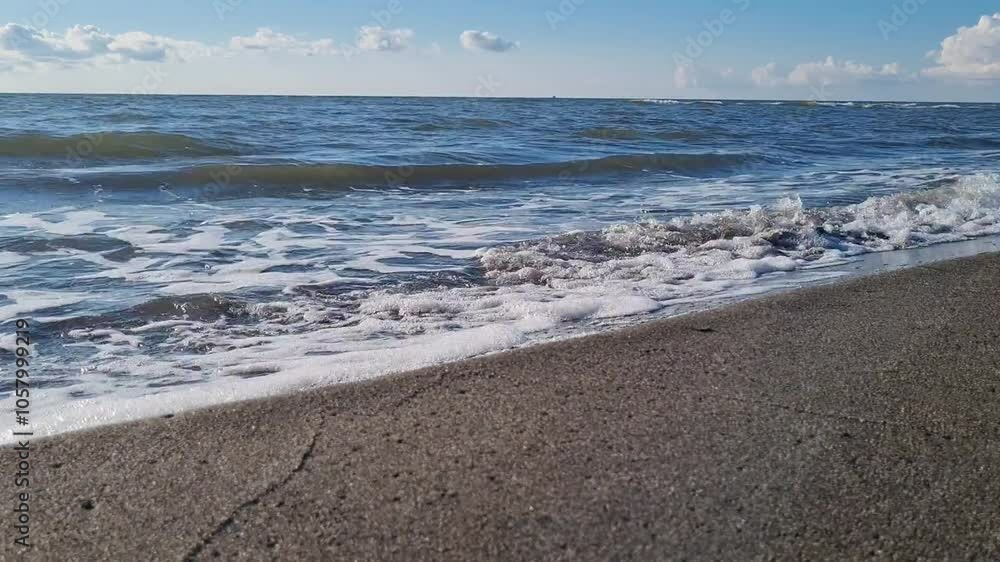 Sea waves roll onto the sandy shore, the glare of the sun plays on the water Sea waves roll onto the sandy shore, the glare of the sun plays on the water