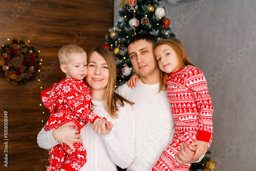 The family in festive red pajamas, are having fun and embracing by the Christmas tree