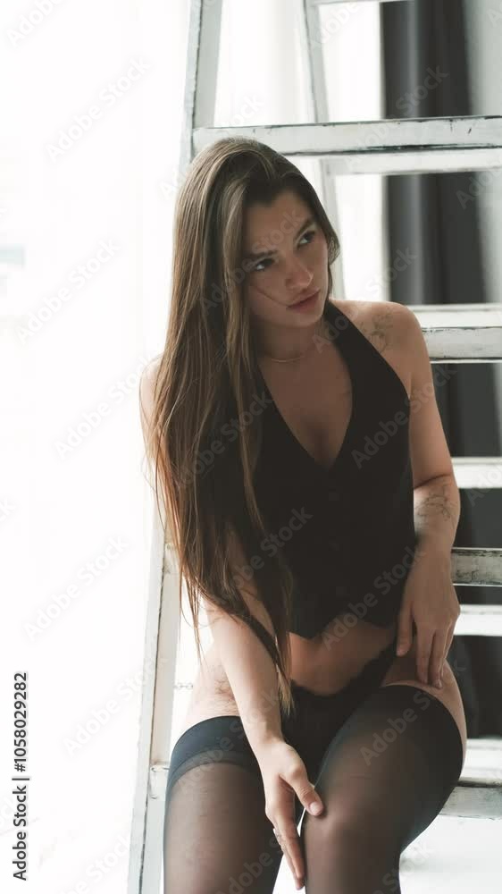 Portrait of young beautiful model posing in black lingerie and stockings near a large window. Calm cute brunette in fashionable lingerie. Portrait of young beautiful model posing in black lingerie and stockings near a large window. Calm cute brunette in fashionable lingerie.