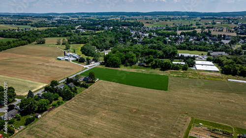 Foto The landscape showcases a vibrant patchwork of green fields and brown farmland stretching toward a small town under a clear blue sky, typical of Pennsylvania's rural charm