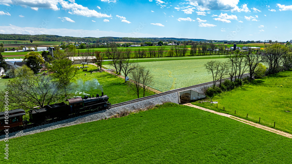 A steam locomotive moves along tracks bordered by vibrant green fields and trees under a clear blue sky. The scenic view captures the charm of countryside rail travel. A steam locomotive moves along tracks bordered by vibrant green fields and trees under a clear blue sky. The scenic view captures the charm of countryside rail travel.