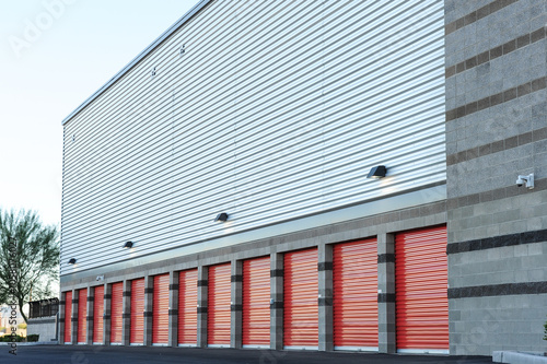 Canvastavla A row of exterior storage units with red roll-up doors lines the side of a moder