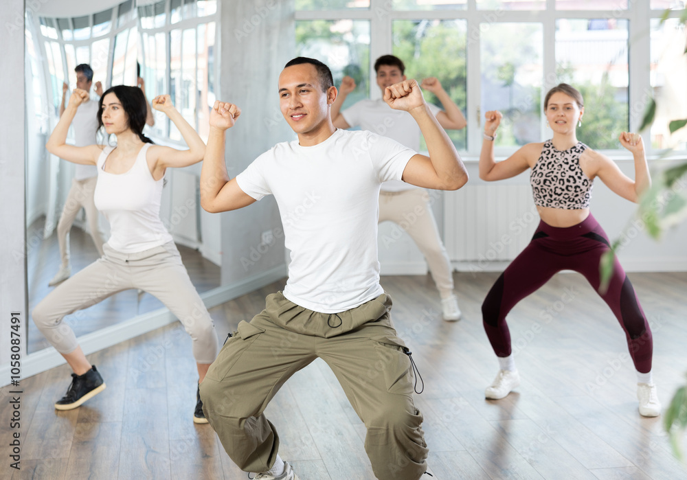 Fototapeta premium Expressive Asian guy honing hip-hop dance moves in mirrored choreographic studio setting during group training..