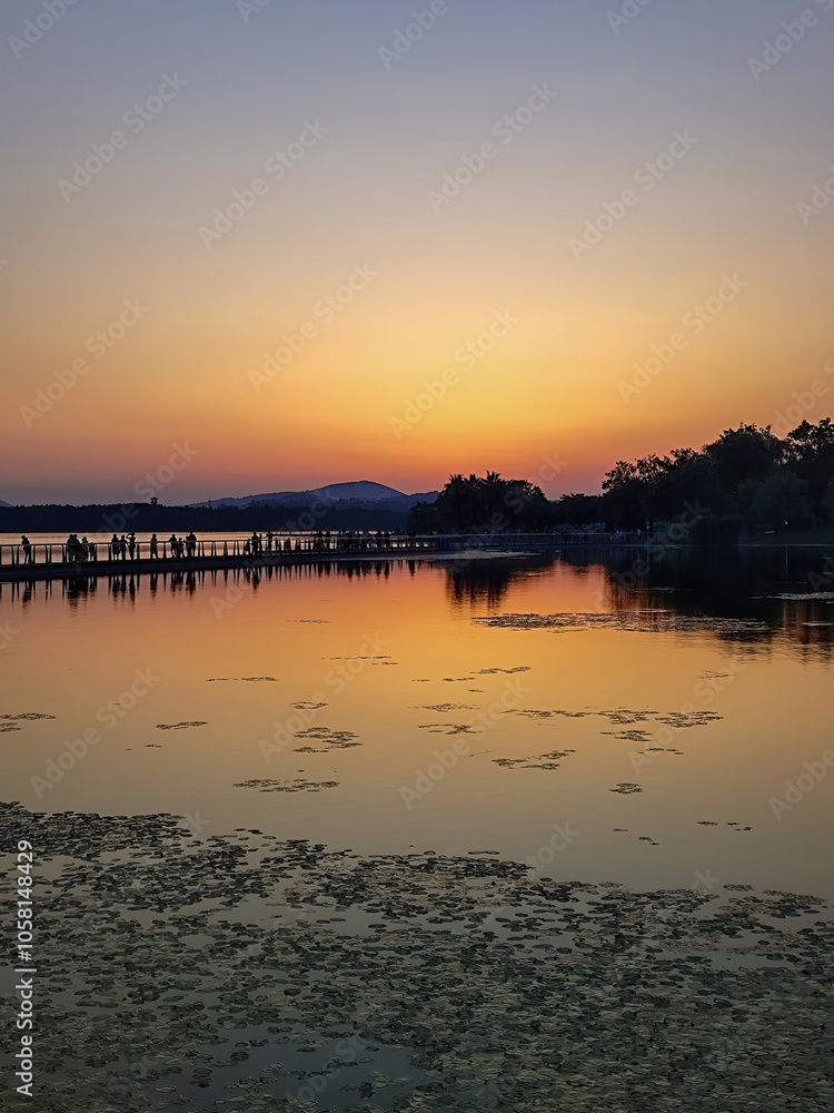 Serene Sunset Over Tranquil Lake with Reflections and Silhouetted Figures Serene Sunset Over Tranquil Lake with Reflections and Silhouetted Figures