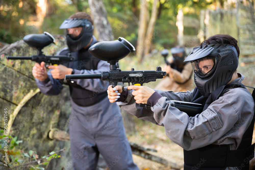 Fototapeta premium Paintball players aiming and shooting with guns at opposing team outdoors