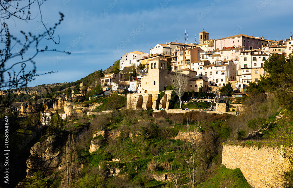 Fototapeta premium Scenic view of Cuenca cityscape on rocky ledge overlooking oldest Catholic parish church of San Miguel on sunny spring day, Spain..