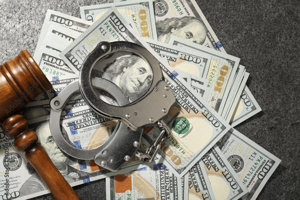 Handcuffs with dollar banknotes and wooden gavel on grey textured table, flat lay Handcuffs with dollar banknotes and wooden gavel on grey textured table, flat lay