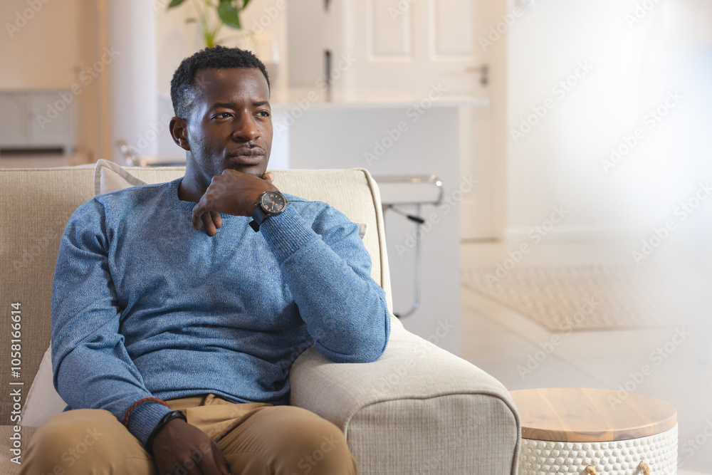 Thoughtful African American African american man relaxing on sofa at home, wearing blue sweater Thoughtful African American African american man relaxing on sofa at home, wearing blue sweater