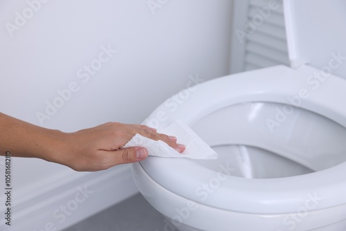 Woman wiping toilet seat with paper in bathroom, closeup